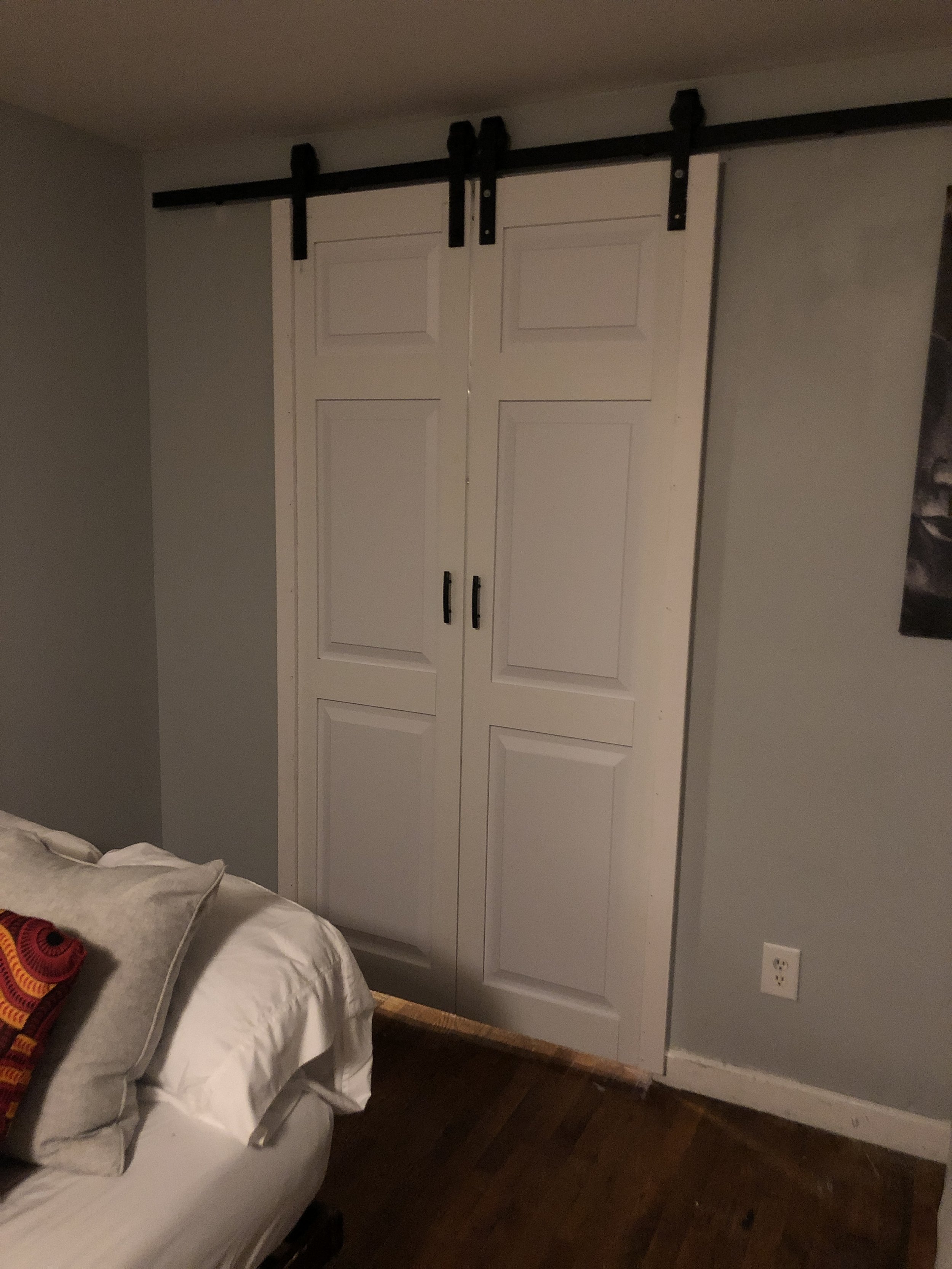 White sliding barn doors on black hardware installed in a modern bedroom in Queens. Professional mounting and installation services.
